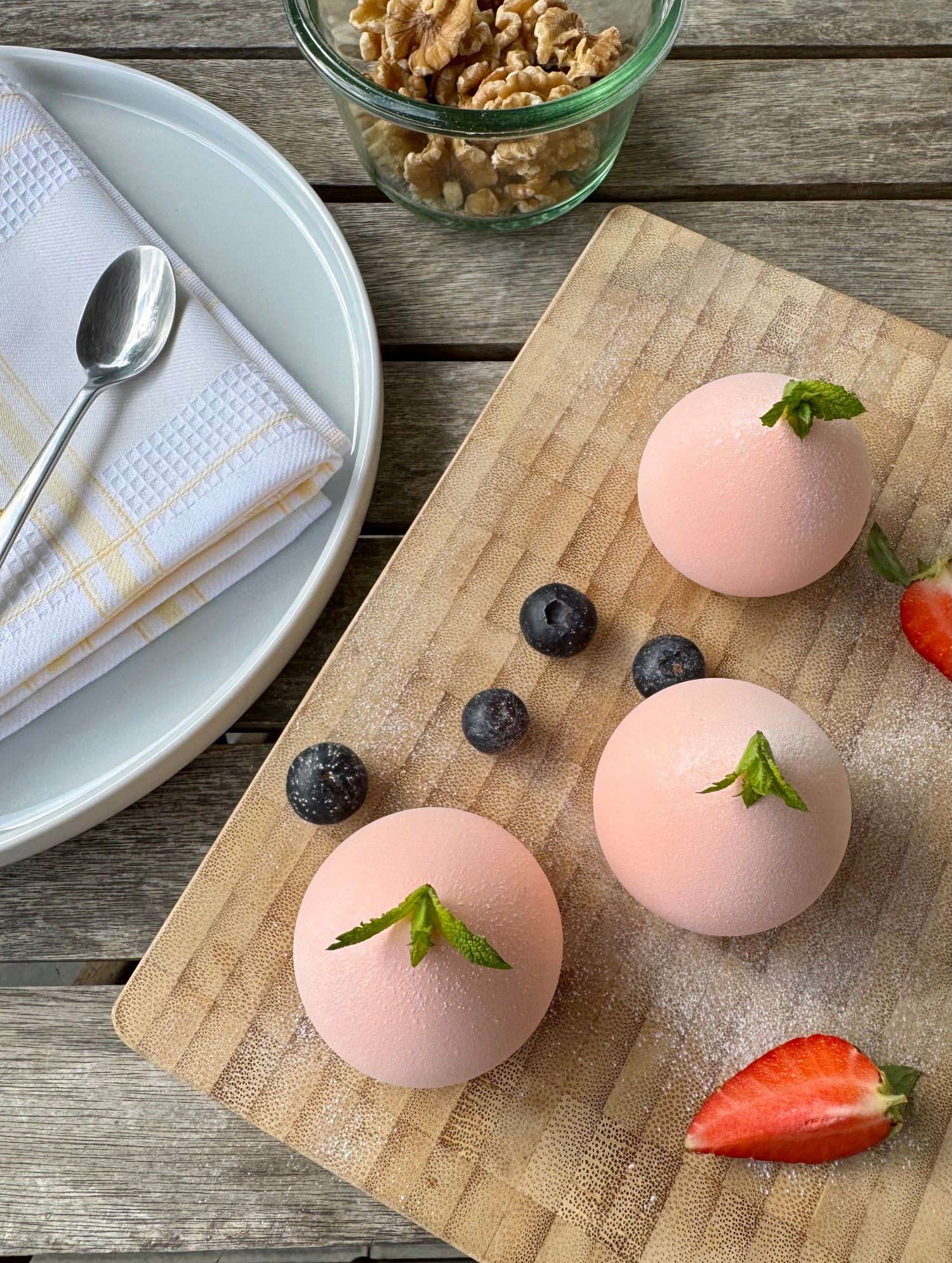 Pink mochi-shaped makeup sponges styled on a wooden board with berries, resembling a dessert scene.